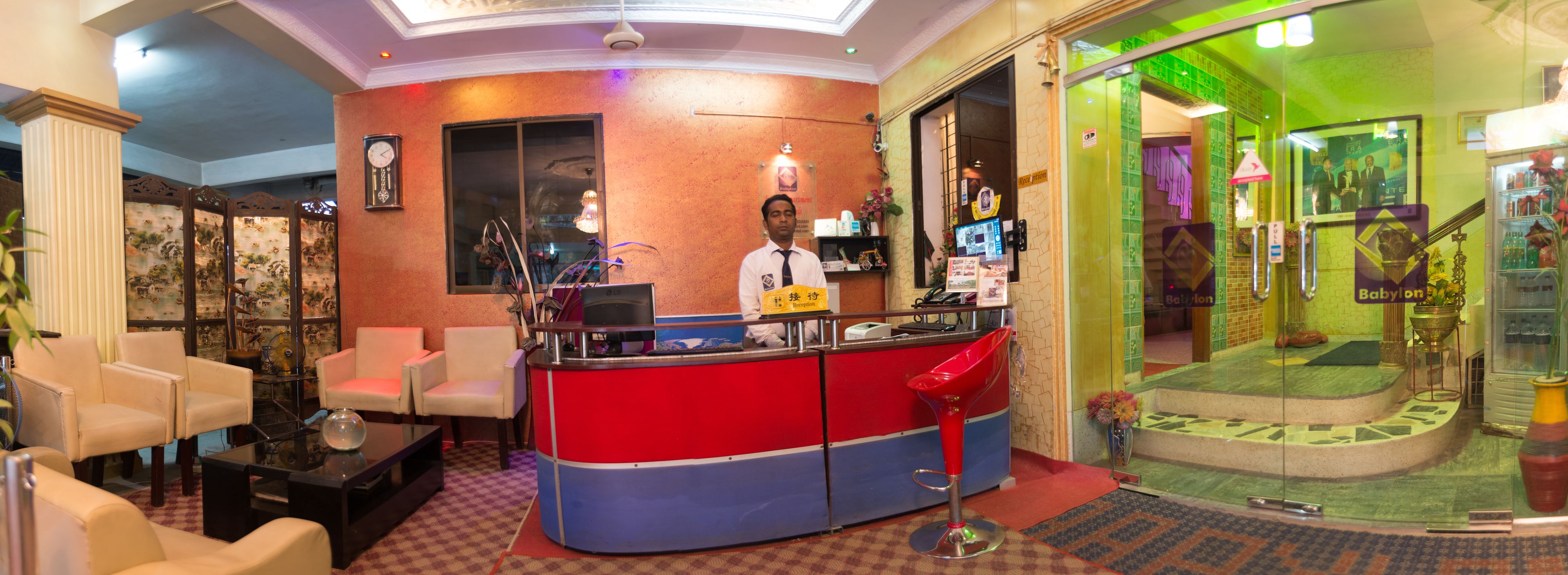 Een receptie met een rode en blauwe balie, een klok en een bar met een televisie.