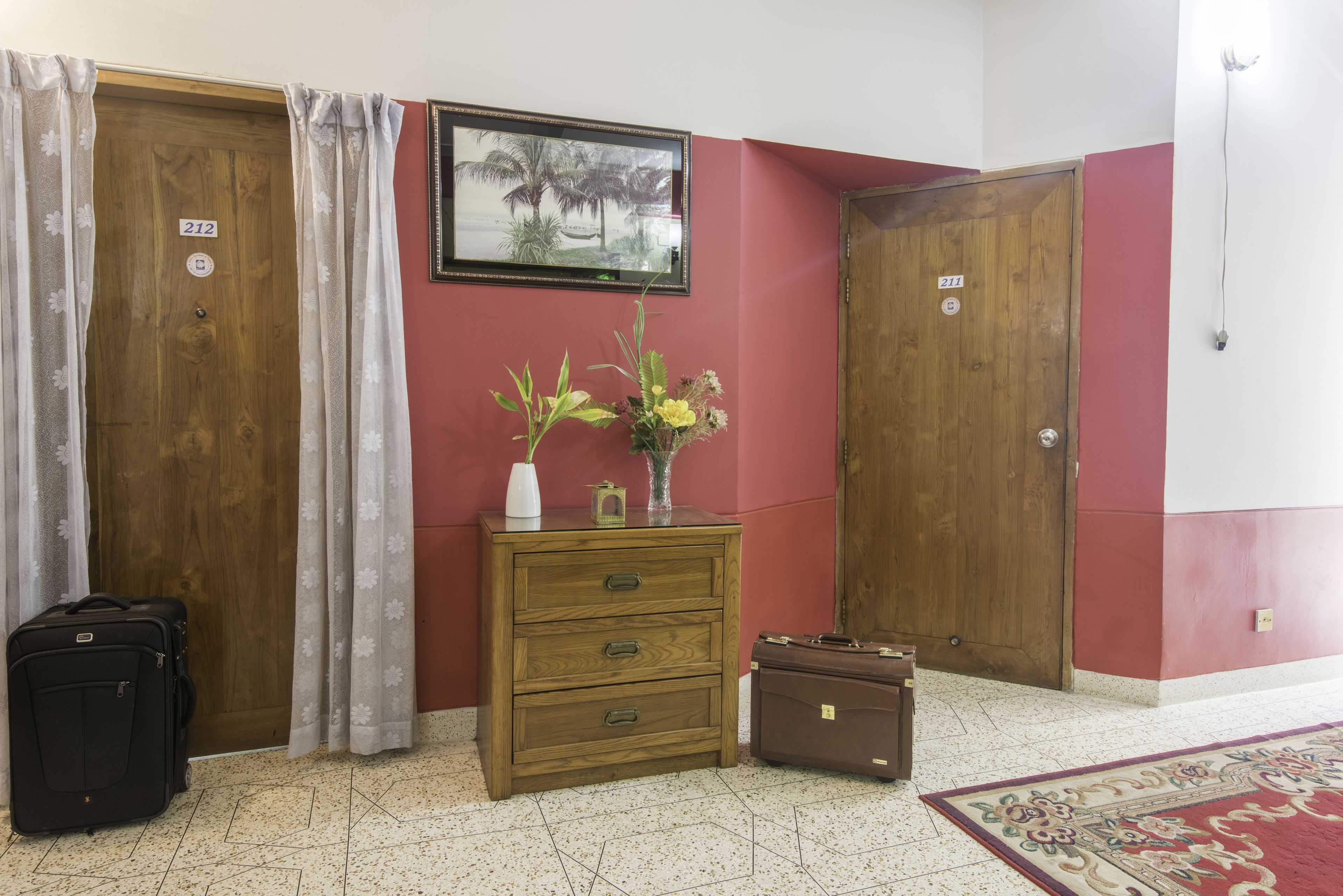 A room with a wooden dresser, two doors, a framed picture on the wall, and a tiled floor.