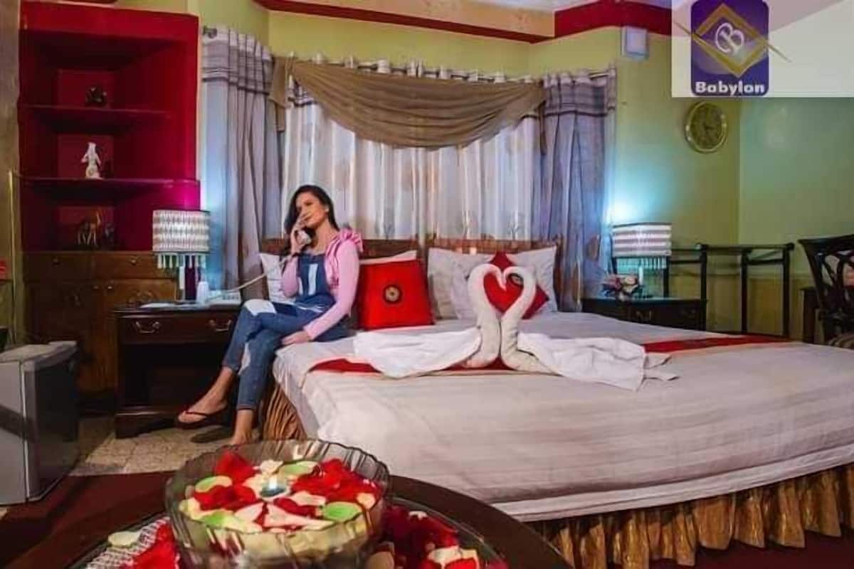 A hotel room with a bed, a desk, a chair, a dresser, and a small table with a bowl of fruit.