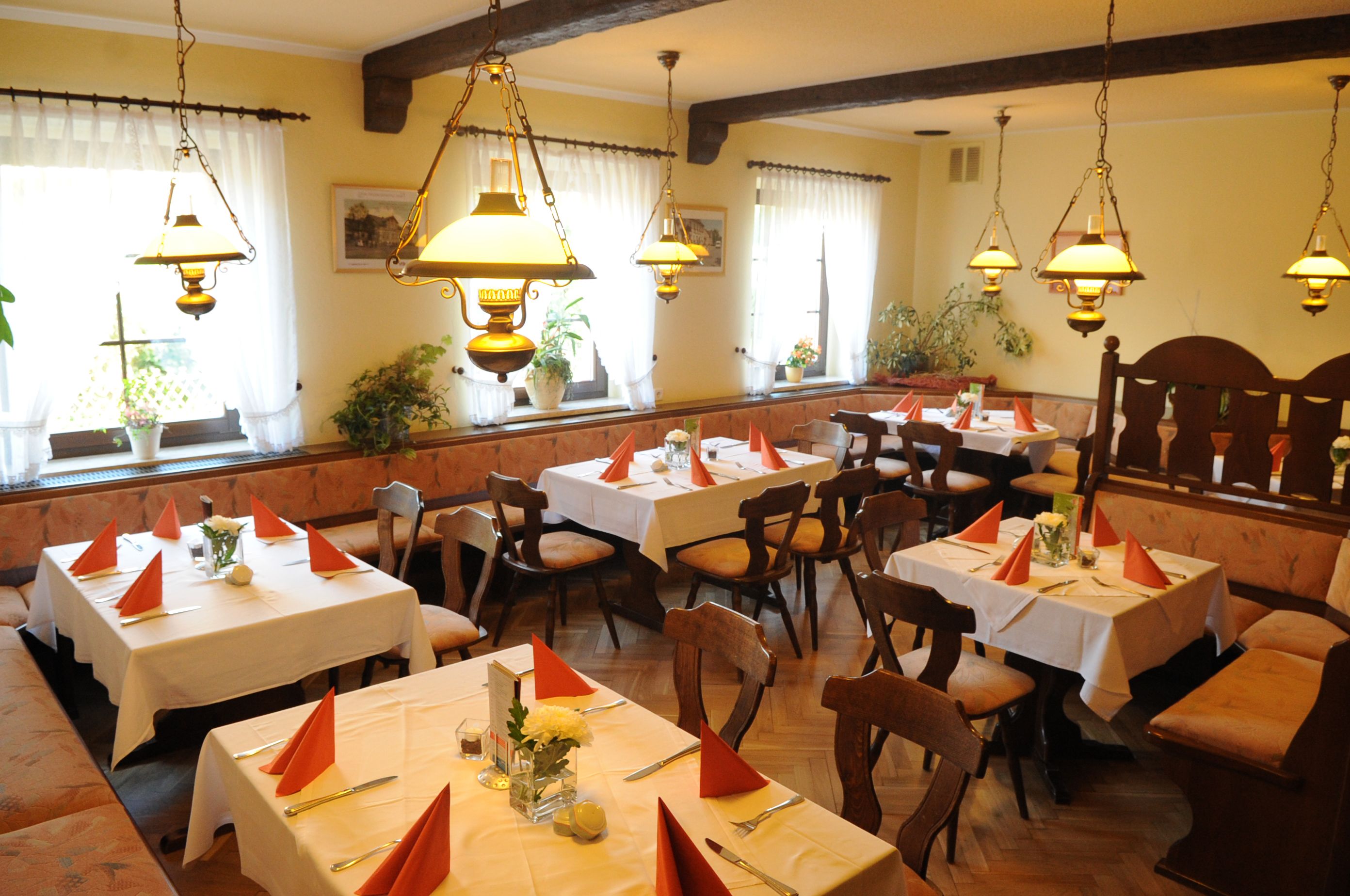 A restaurant with multiple tables set for dining, each with orange napkins and white tablecloths.