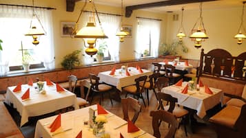 A restaurant with multiple tables set for dining, each with orange napkins and white tablecloths.