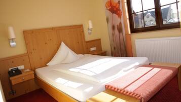 A hotel room with a wooden bed, a bedside table with a lamp, a window with a view of buildings, and a radiator on the wall.