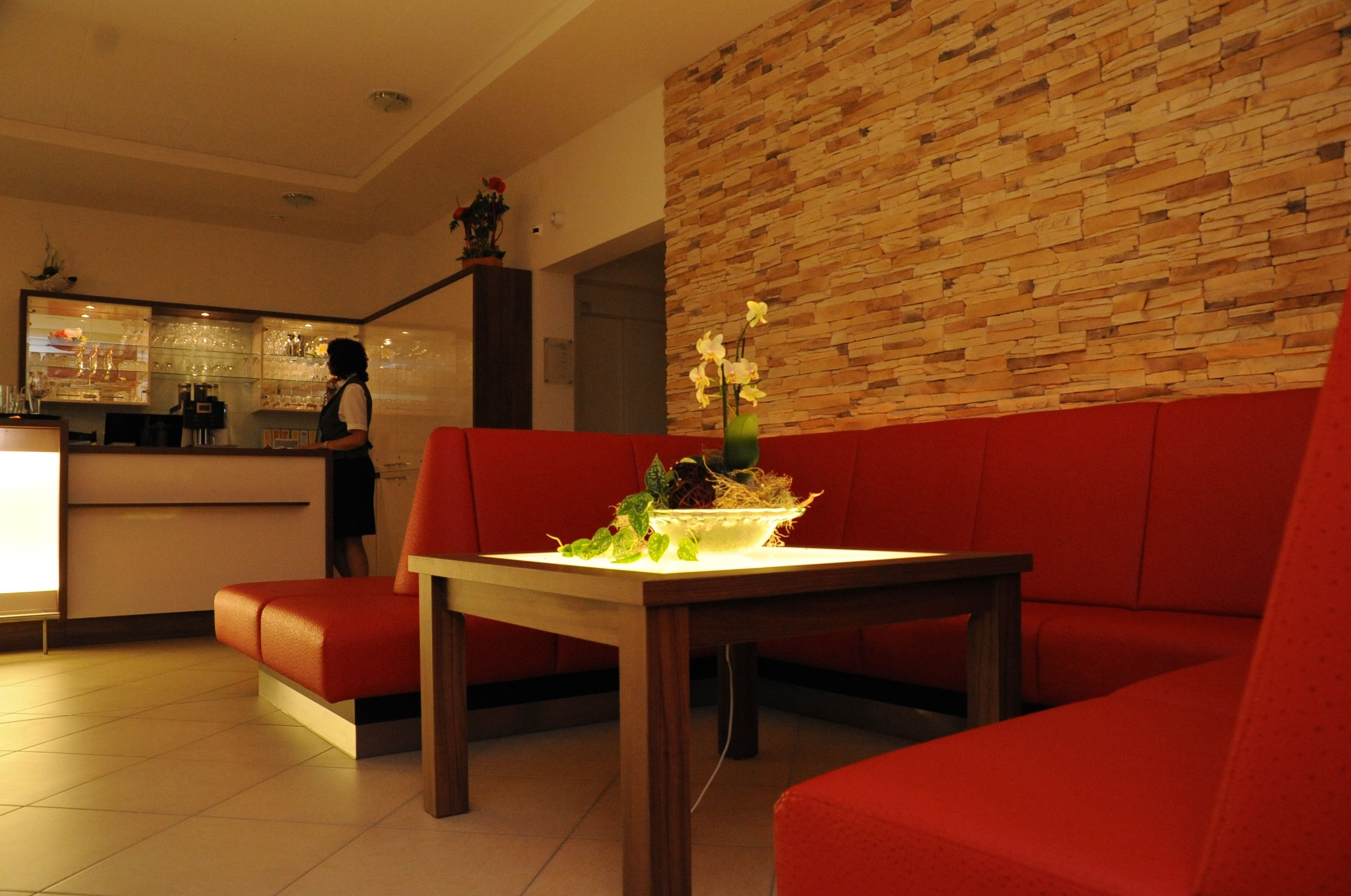 Un intérieur moderne avec un canapé rouge, une table en bois ornée d’un vase, et un coin bar à l’arrière-plan.