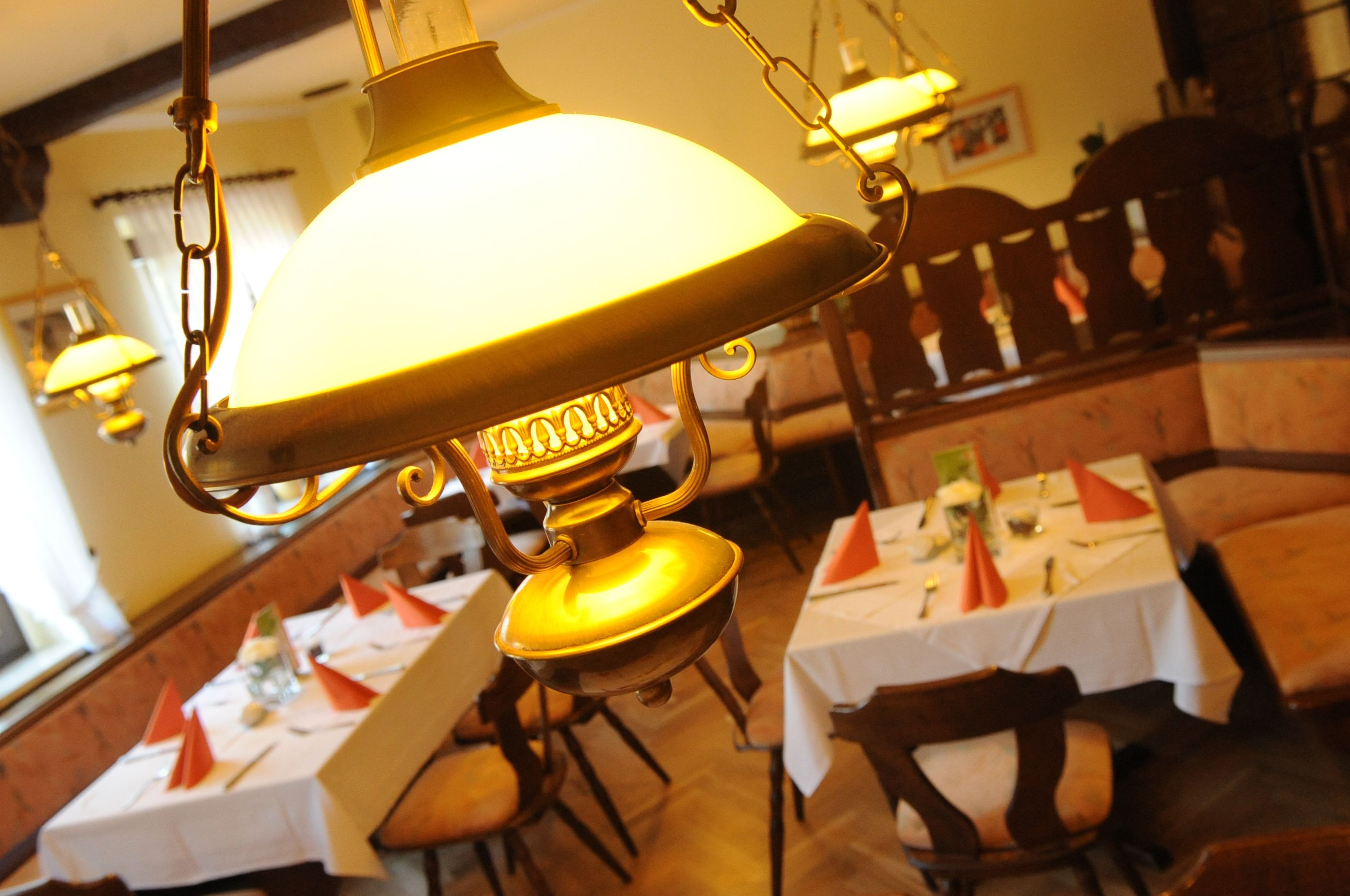A dining area with tables set for service, hanging lamps, and wooden furniture.