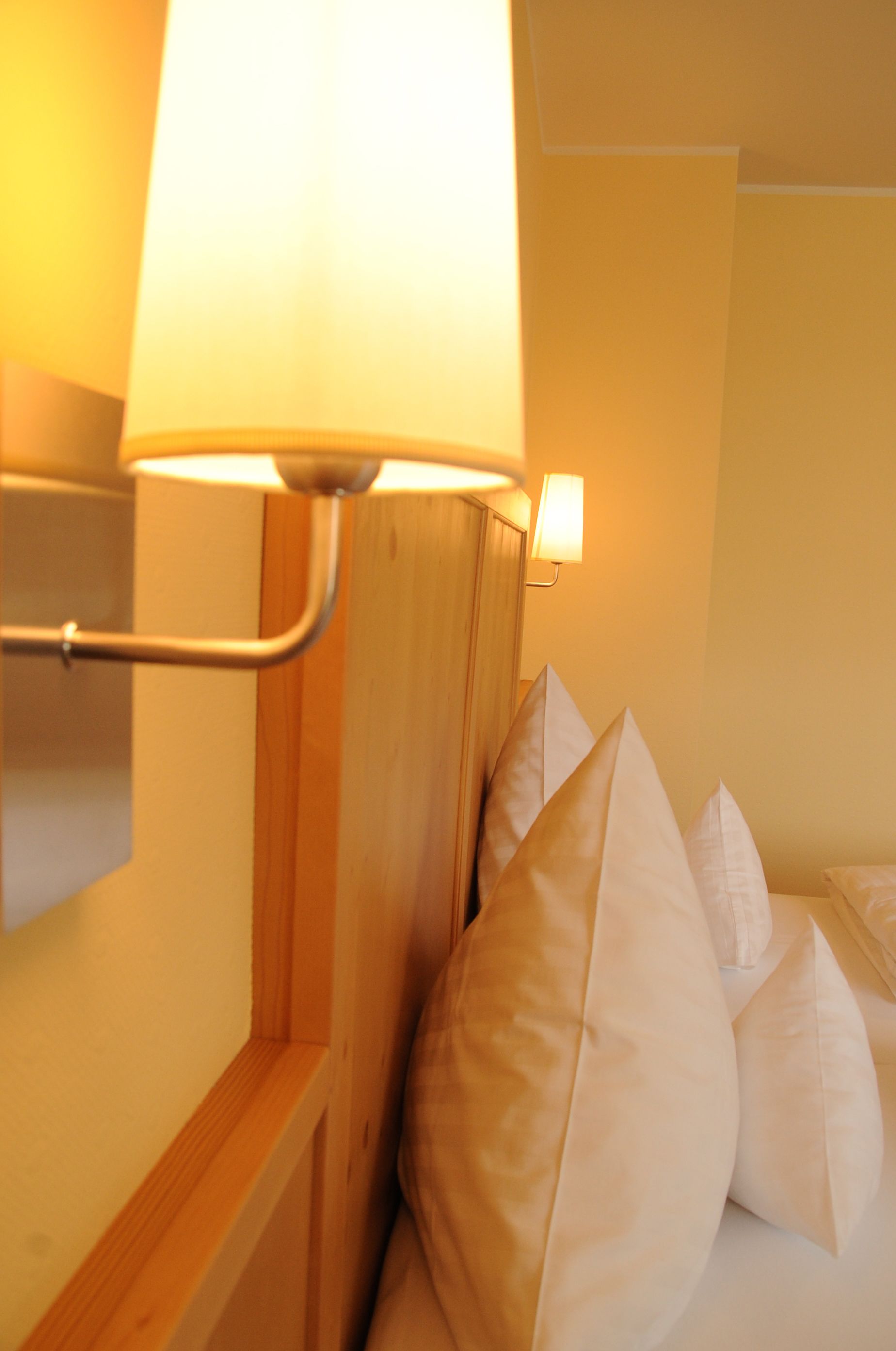 A hotel room with a wooden headboard, a bedside lamp, and several pillows.
