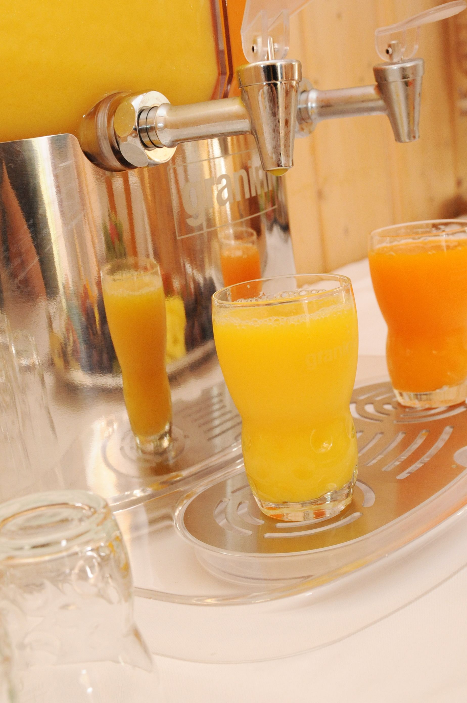 Um dispensador de suco com três copos de sumo de laranja.