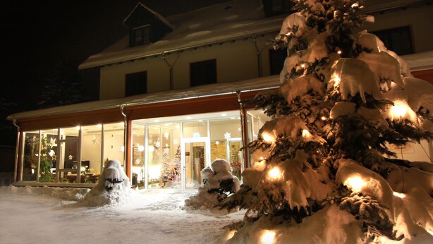 A snow-covered Christmas tree in front of a building with large windows and a snowman statue. - Beierleins Hotel & Catering GmbH (Callenberg)
