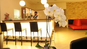 A reception area with a counter, bar stools, a red sofa, and a white orchid. - Beierleins Hotel & Catering GmbH (Callenberg)