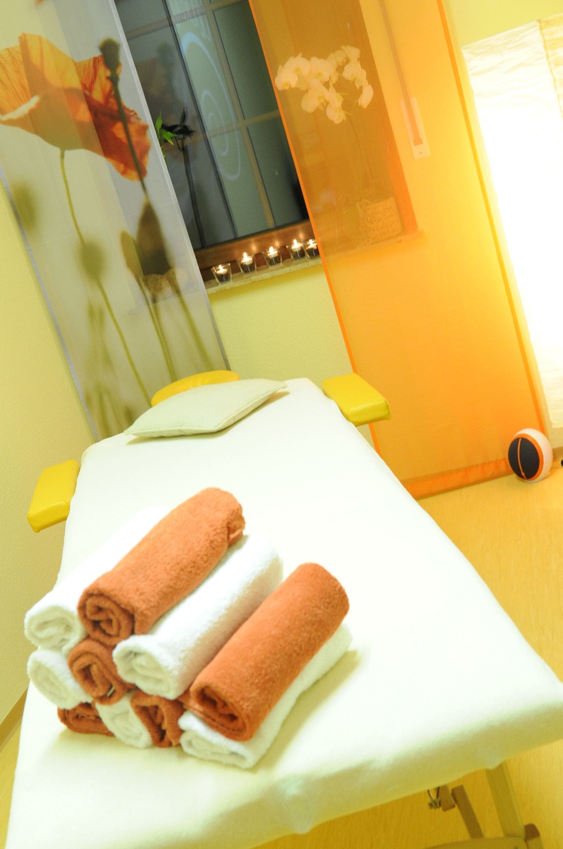 A room with a massage table, towels, a window with a view, and a mirror.