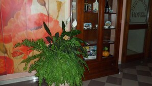 Un hall de hotel con un gran mural floral, un aparador de madera con varios objetos y un suelo a cuadros.