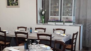 Un comedor con mesas dispuestas para cuatro, un ventanal con cortinas, un cuadro enmarcado en la pared y un armario blanco con puertas de cristal.
