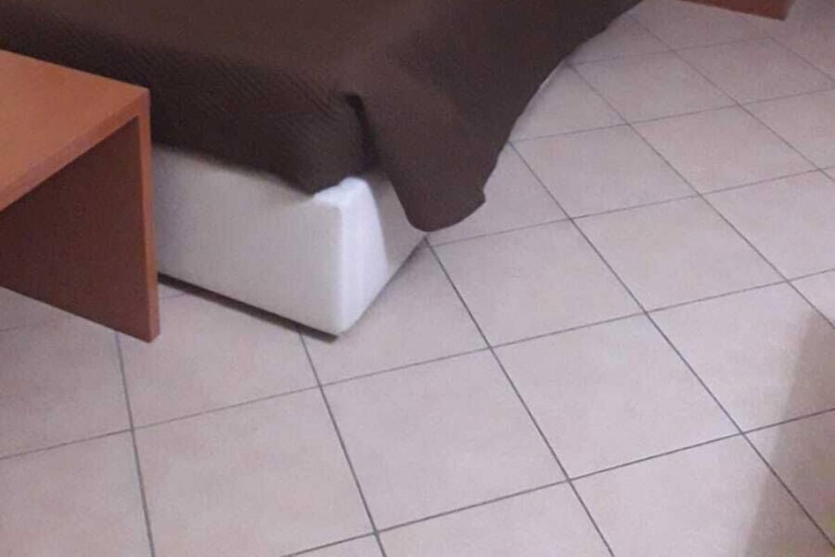 A single bed with a wooden headboard and a white mattress, a nightstand with a lamp, and a small table.