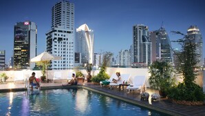 Una piscina al terrat amb gandules i plantes en testos, envoltada d'edificis alts.