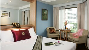 Habitació d'hotel amb un llit gran, una cadira, una taula petita amb un ram i una finestra amb cortines.