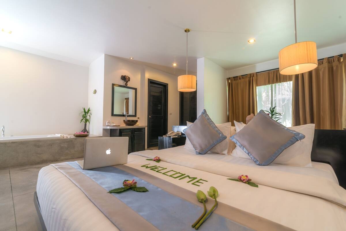 A modern hotel room with a bed, a laptop, a welcome mat, and a view of the outside.