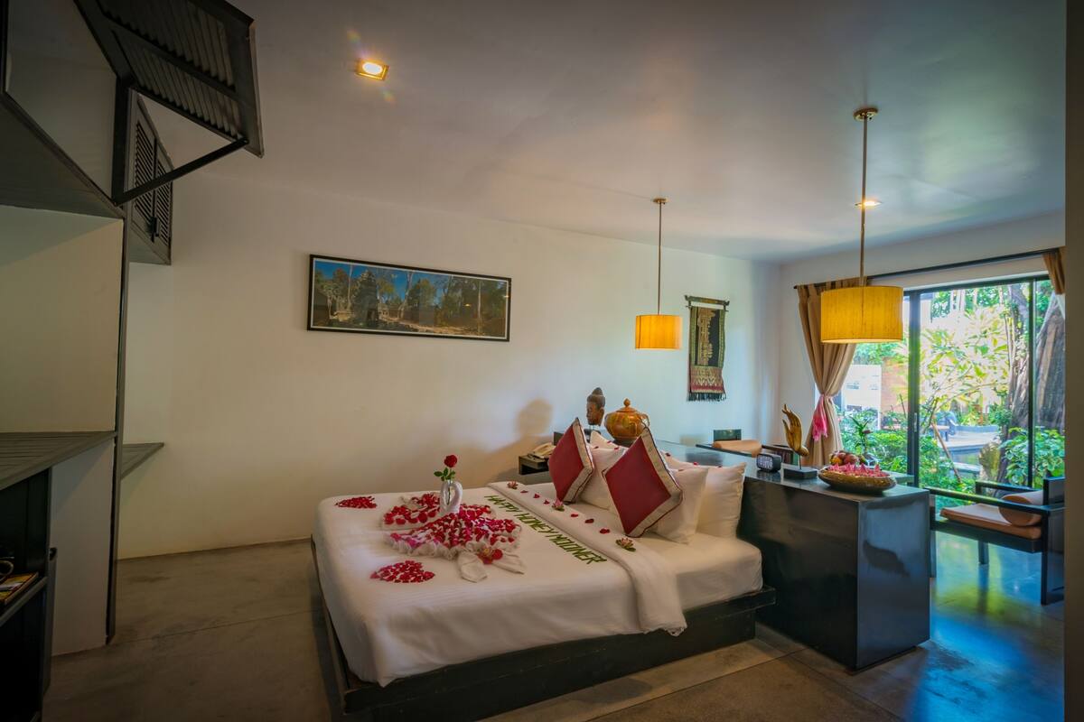 A hotel room with a bed, a desk, and a window with a view of greenery.