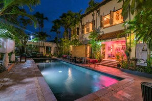 A swimming pool with a tiled deck, surrounded by palm trees and a building with a balcony. - Bunwin Boutique Hotel (Siem Reap)