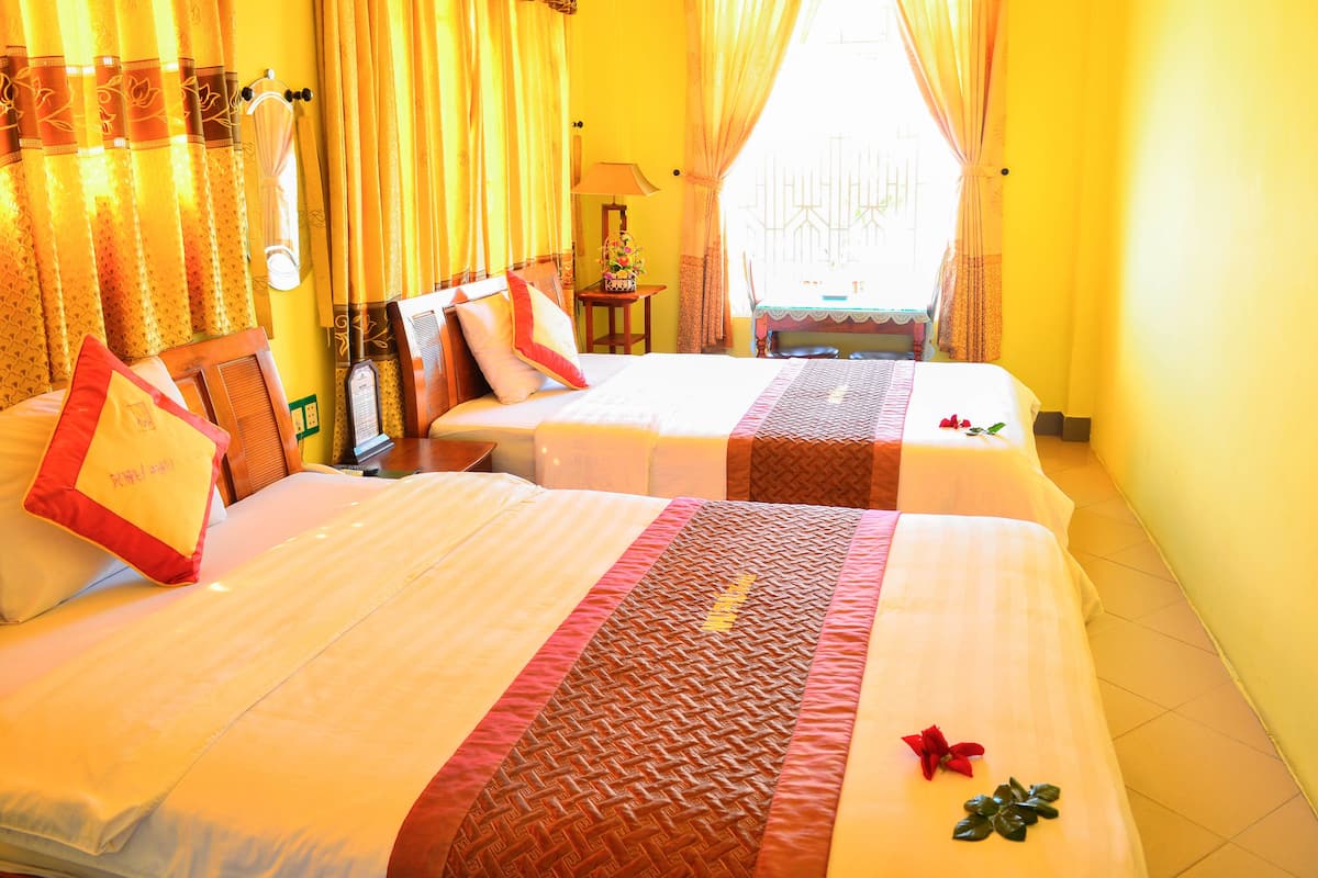Habitación de hotel con dos camas, paredes amarillas y cortinas.