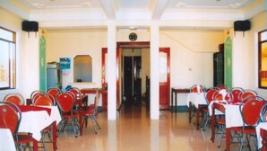 A conference room with rows of red chairs and tables, a clock on the wall, and a door at the far end. - Nhu Phu Hotel (Hue)