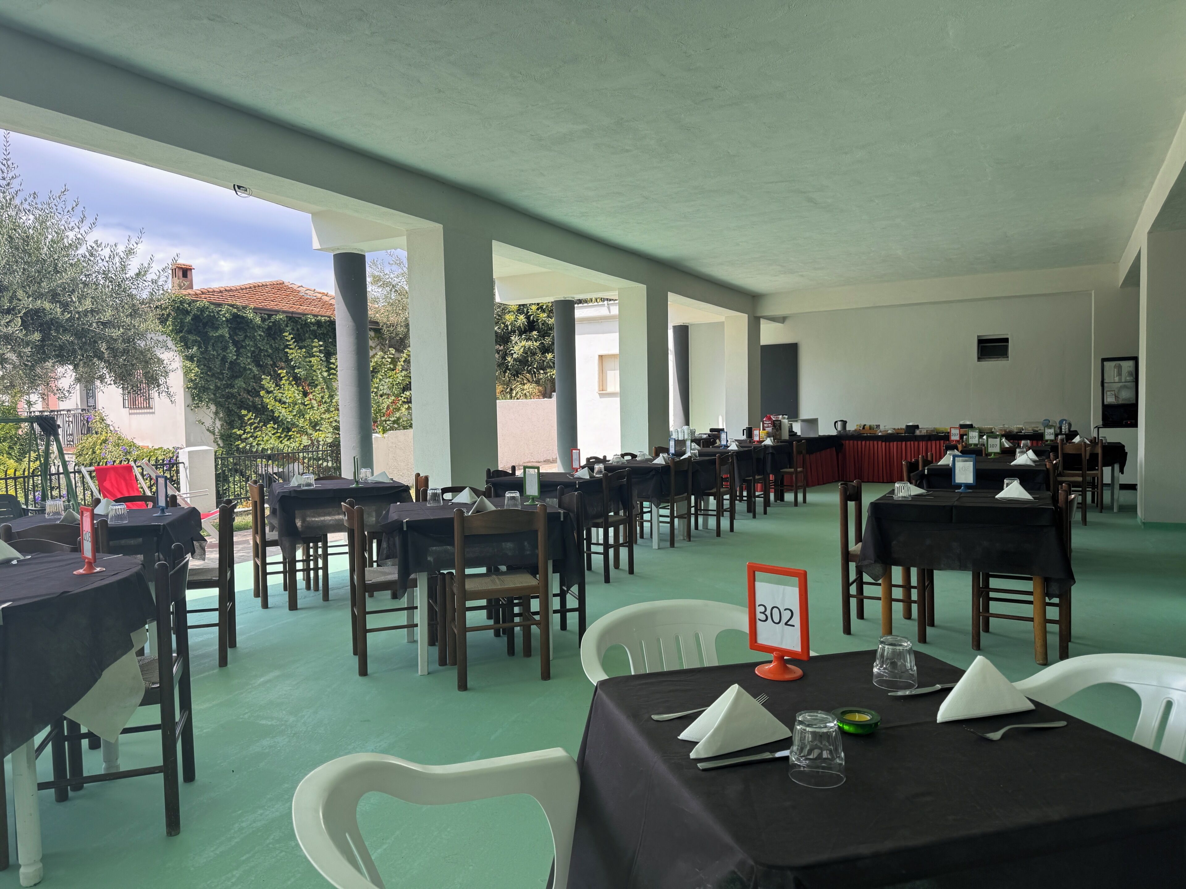 Un vaste espace intérieur aménagé en salle à manger, avec des tables et des chaises, une vue sur l’extérieur et un panneau indiquant le numéro de la table : 302.