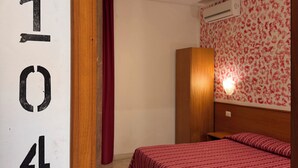 Una habitación con cama, armario, cortina y pared decorada con papel tapiz floral.