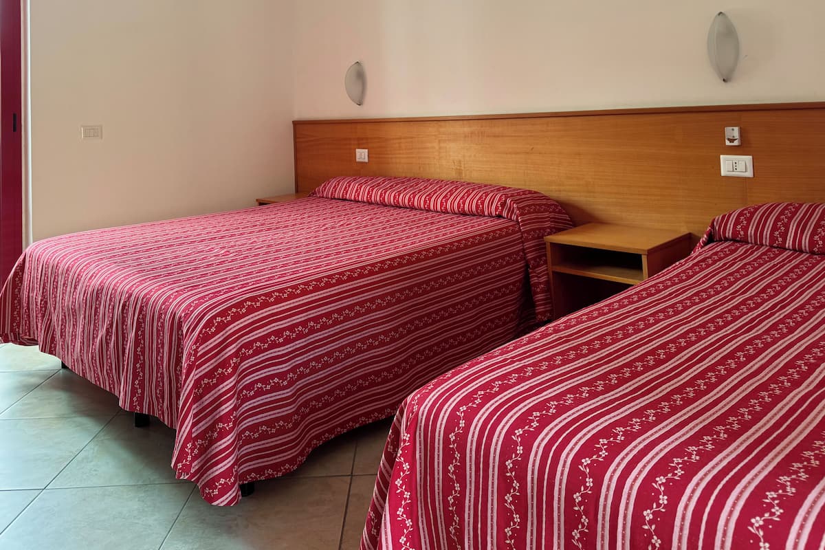 Habitación con dos camas individuales, cabeceros de madera y una mesita de noche pequeña de madera.