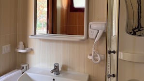 Un baño con lavamanos, espejo, secador de pelo y puerta de ducha.