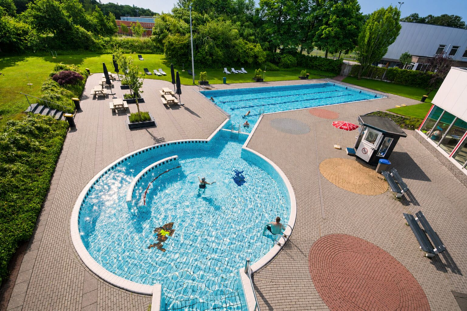 A swimming pool with a circular section and a rectangular section, surrounded by lounge chairs and umbrellas.