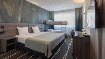 A hotel room with a bunk bed, a desk with a lamp, a TV, and a large window with curtains.