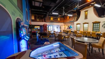 Un grand espace intérieur aménagé avec plusieurs tables et chaises, un billard et des jeux d’arcade.