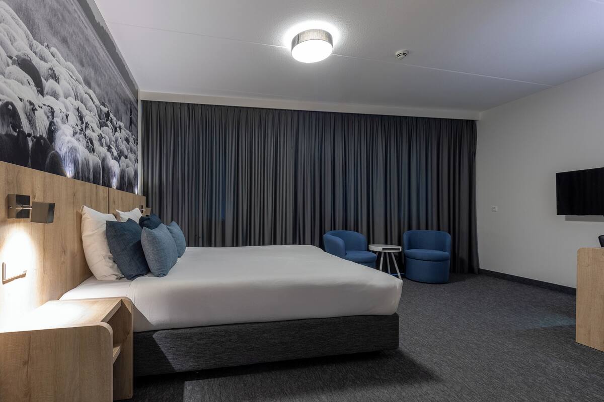 Une chambre d’hôtel moderne dotée d’un grand lit, d’une télévision à écran plat, d’un bureau et d’un coin salon avec deux fauteuils.