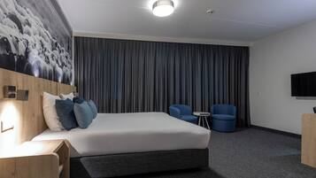 A modern hotel room with a large bed, a flat-screen TV, a desk, and a seating area with two chairs.