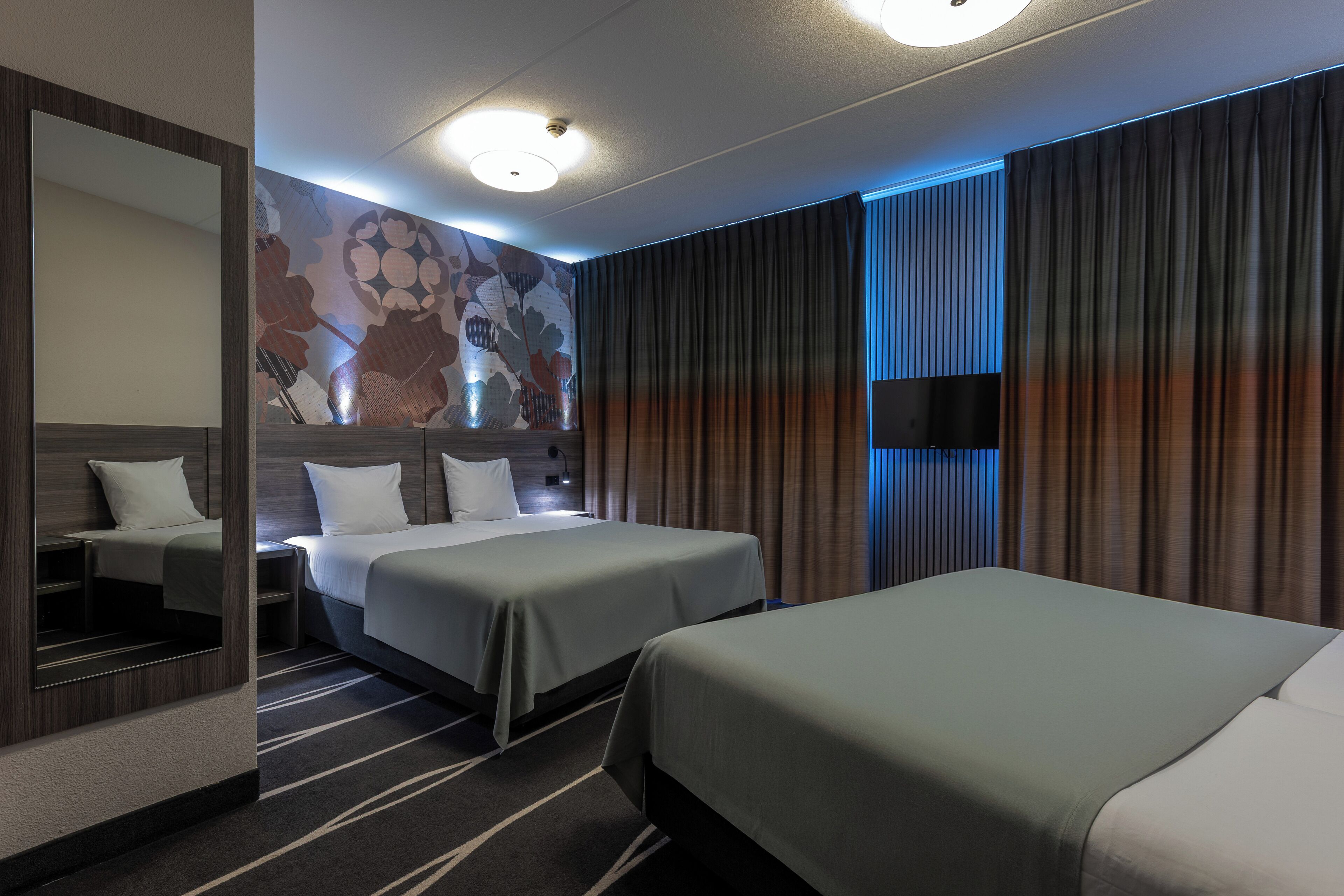 A hotel room with two beds, a large mirror, a flat-screen TV, and a decorative wall.