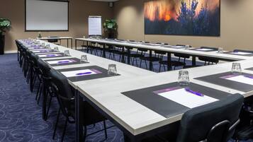 Une salle de conférence avec de longues tables, des chaises, un écran de projection et un grand tableau abstrait au mur.