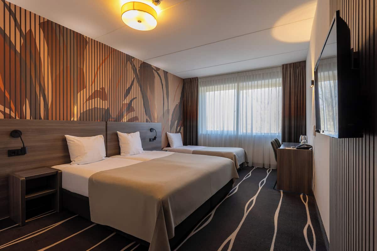 Une chambre d’hôtel avec deux lits, un bureau, une chaise, une télévision et une fenêtre avec des rideaux.