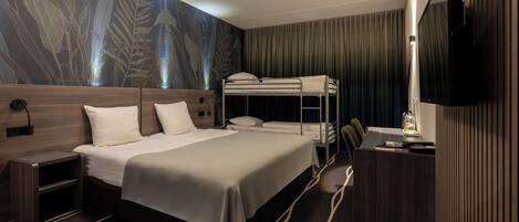 A hotel room with a bunk bed, a desk with a chair, a TV mounted on the wall, and a patterned wallpaper.