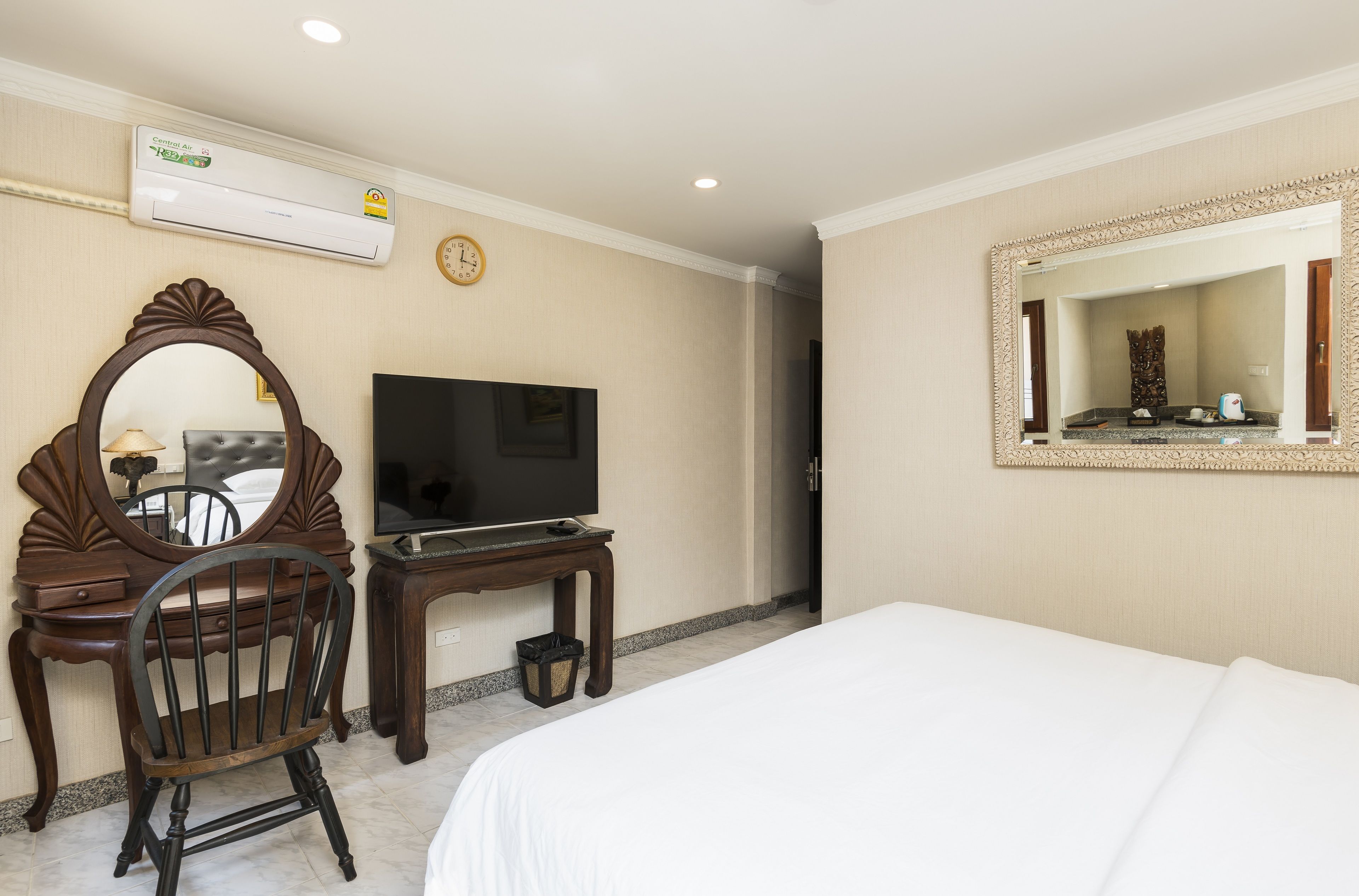 A hotel room with a bed, a television, a desk with a chair, a mirror, and an air conditioning unit.