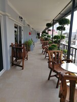 Un espacio de estar al aire libre cubierto con sillas y mesas de madera, plantas en macetas y vistas a la ciudad.