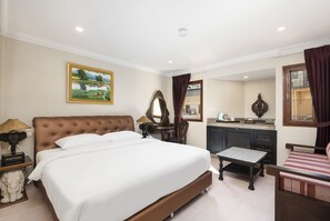 A hotel room with a large bed, a small table, a desk, a mirror, and a painting on the wall. - The Ambiance (Pattaya)