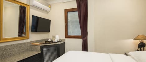 A hotel room with a bed, a TV, a mirror, a dresser, a window with curtains, and a lamp.