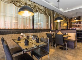 Un restaurante con una decoración moderna, que cuenta con una zona de bar con una selección de vinos, un área de comedor con mesas y sillas, y vistas a través de amplios ventanales con cortinas.