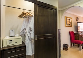 Habitación de hotel con un armario de madera, una bata blanca colgada en un perchero, una silla roja y un escritorio con televisor.