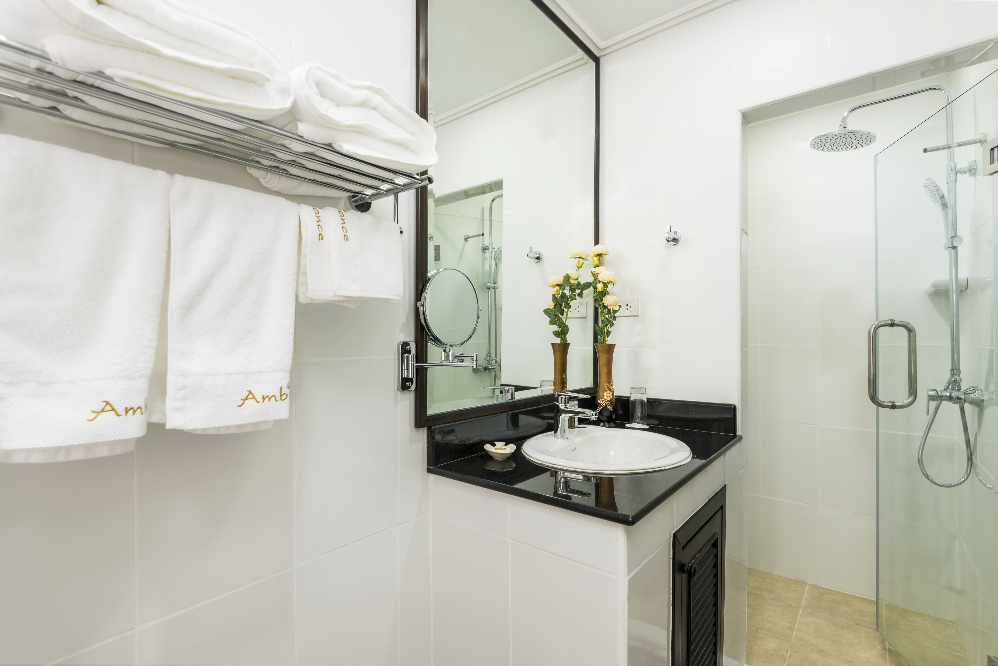 A modern bathroom with a glass shower enclosure, a black countertop sink, and white tiled walls.
