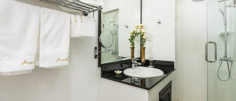 A modern bathroom with a glass shower enclosure, a black countertop sink, and white tiled walls.