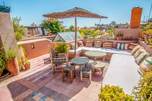 A rooftop patio with a seating area, including a sofa, chairs, and a table. There are potted plants and a pergola providing shade. - Riad Chorfa (Marrakech)