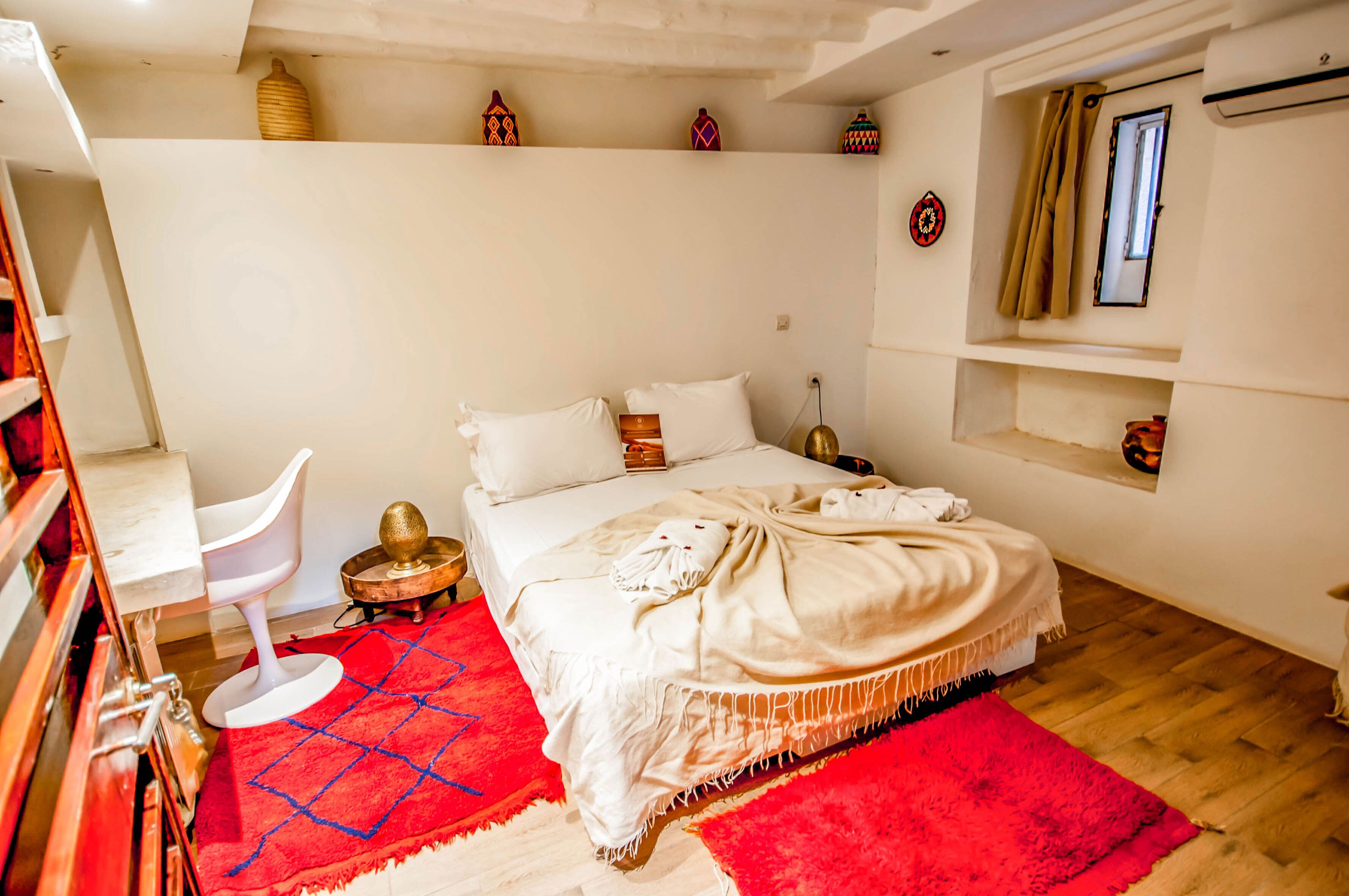 A bedroom with a bed, a red rug, a white chair, and decorative items on the wall.