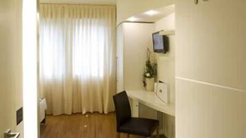 A hotel room with a wooden floor, a desk with a chair, a television, and a number '103' on the wall.