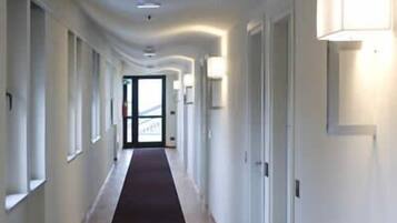 A long, narrow hallway with a dark carpet, white walls, and doors on both sides.