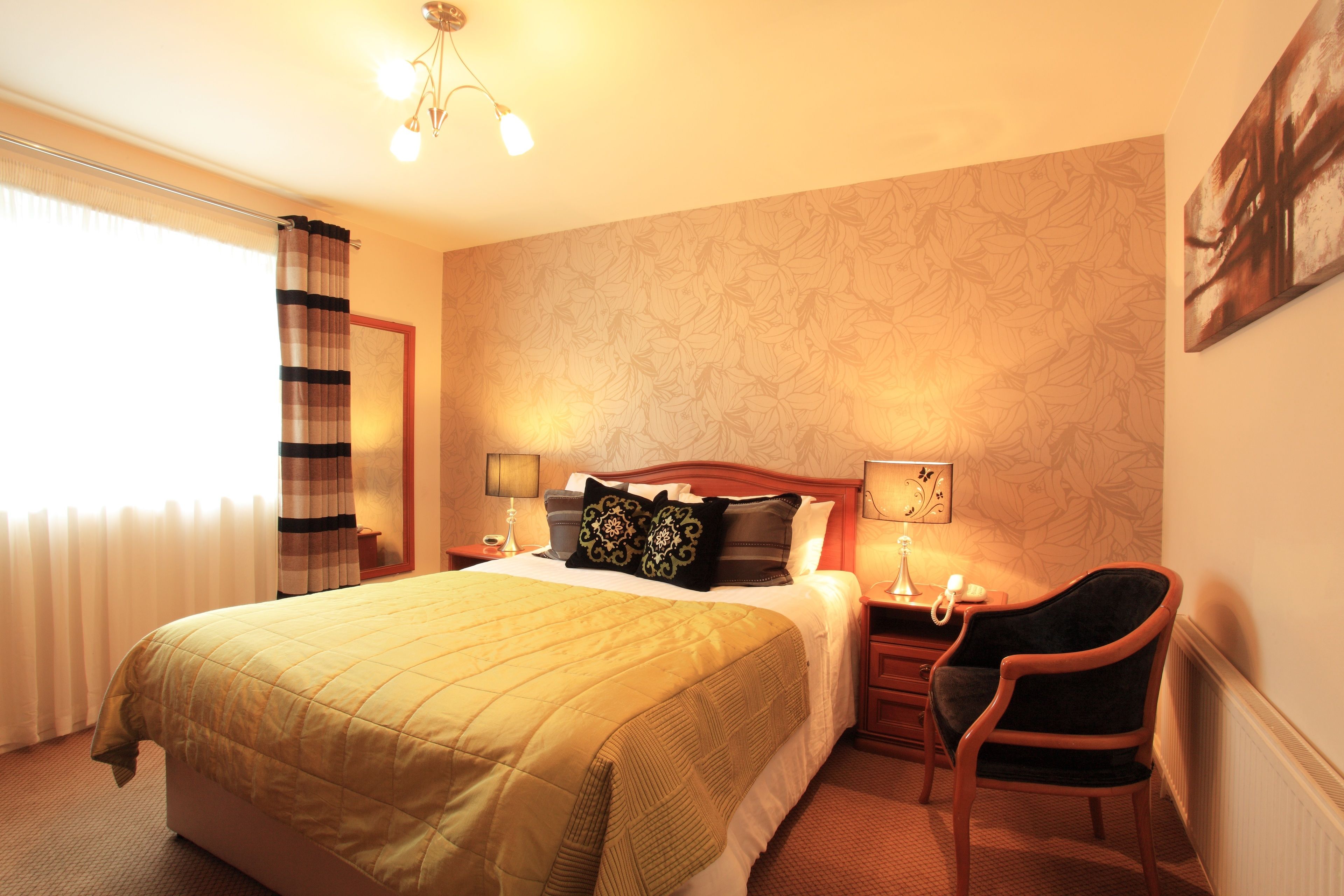 Een hotelkamer met een bed, een stoel, een nachtkastje, een lamp en een raam met gordijnen.