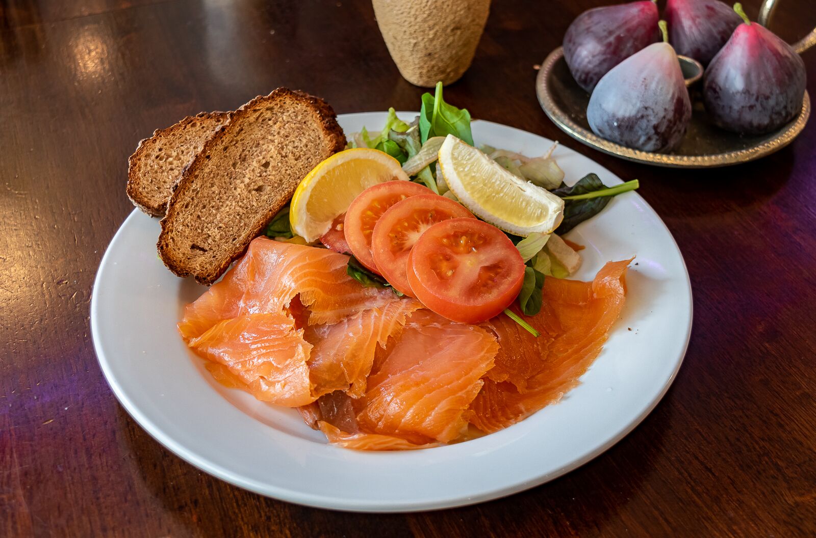 A plate of smoked salmon with bread and salad on a wooden table.